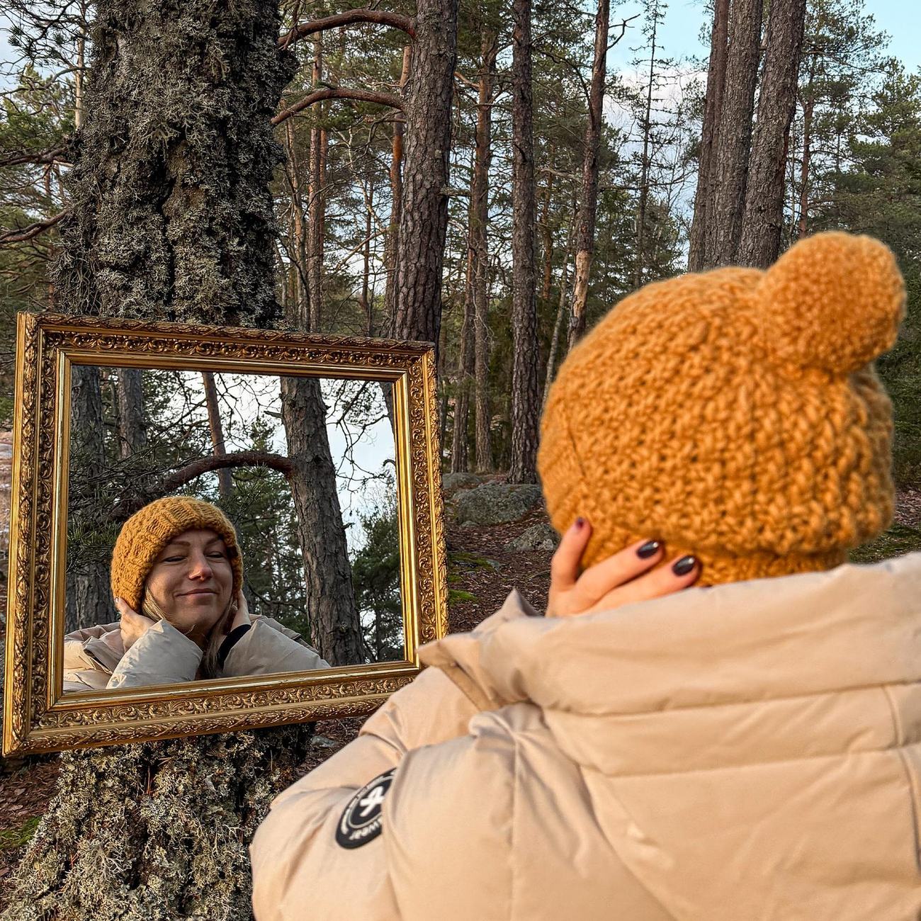 Looking into the mirror hung on a pine, wearing the yellow beanie