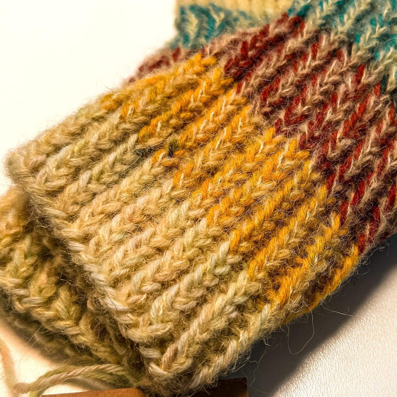 Close-up of gold, rust and teal stitches in a hand-knitted sock cuff