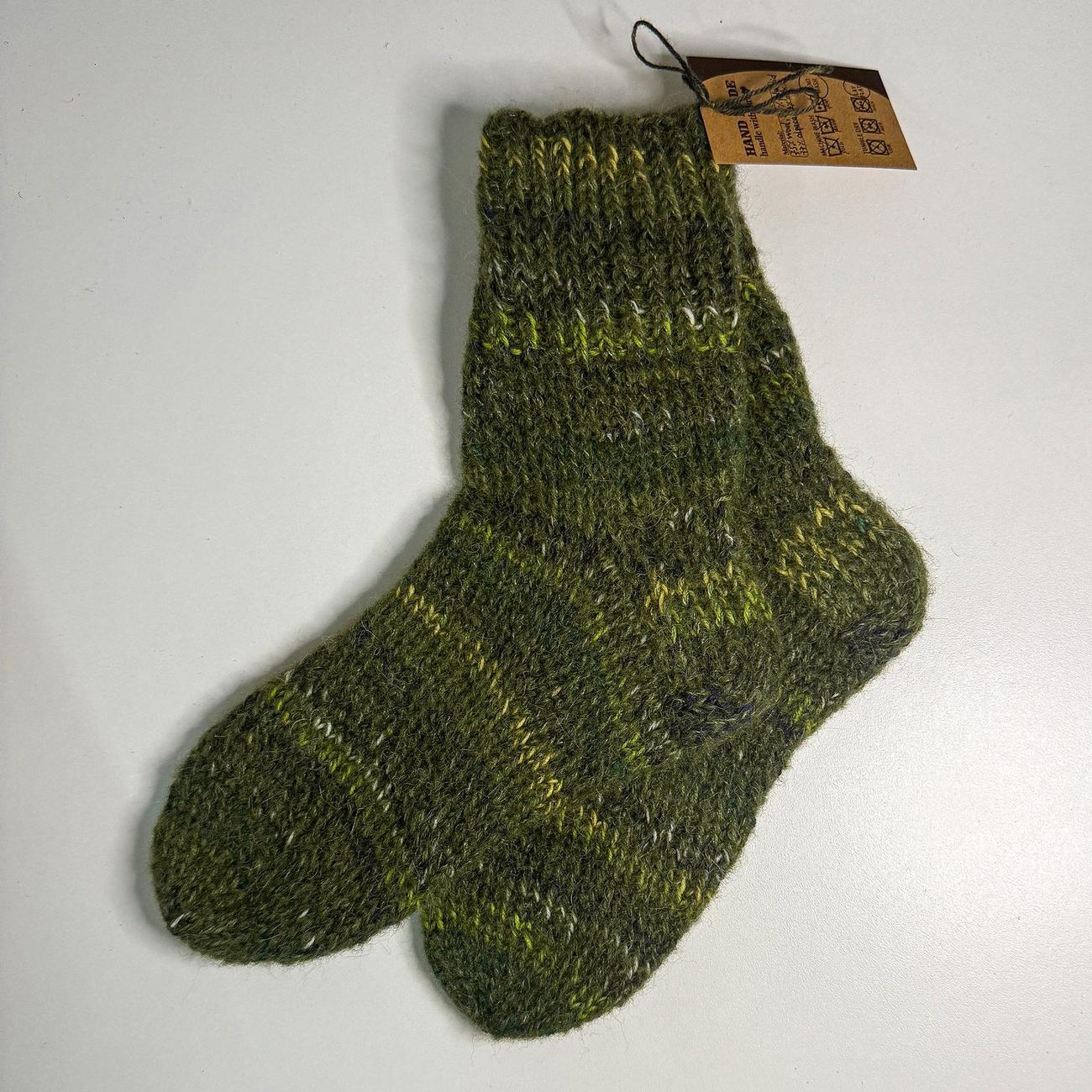 Forest green melange socks with yellow and lime flecks, laid flat with the handmade tag