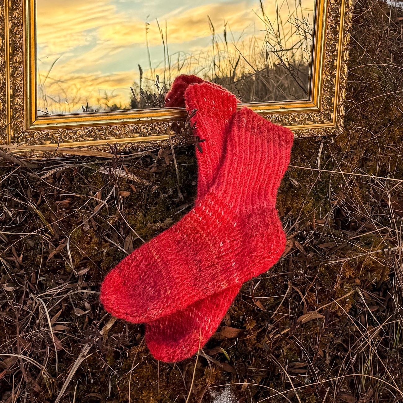Bright red socks on frosted moss, a sunset sky caught in the mirror