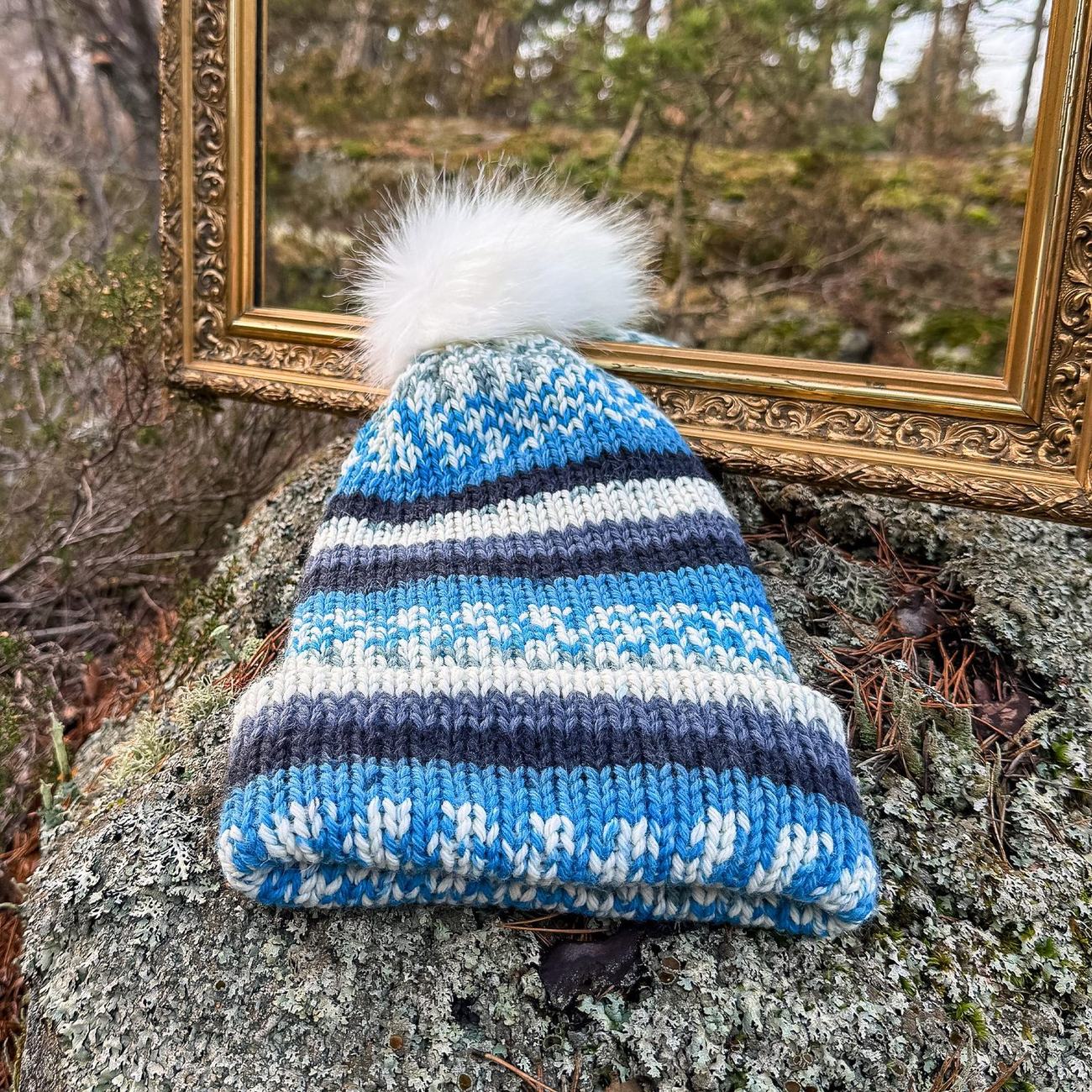 The blue striped beanie on a lichen covered rock in front of the mirror