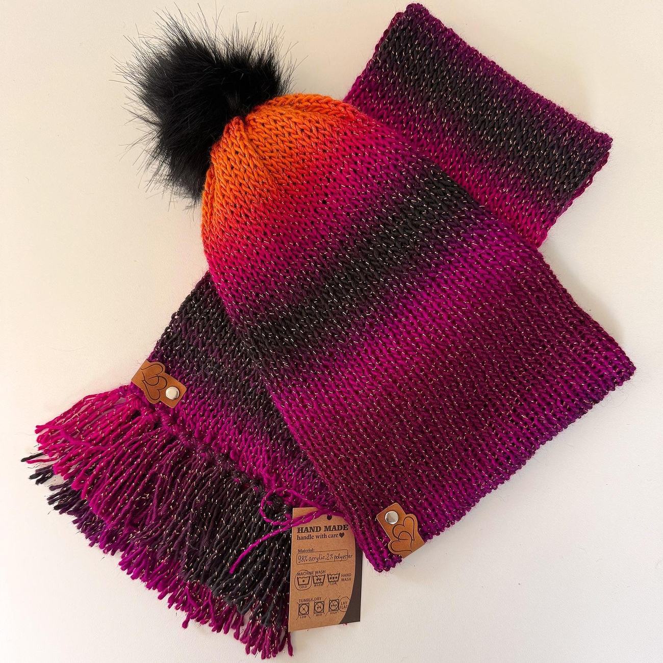 Beanie and scarf set in the Magenta to Midnight gradient, orange fading through magenta to deep plum, with a black faux-fur pom and leather tags